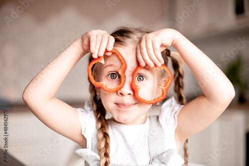 Portrait of overjoyed little girl make funny faces with vegetable, happy child have fun cooking, preparing food in kitchen. Healthy food, natural vitamins, baby dieting concept
