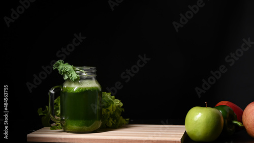 Glass of green vegetable smoothie with ingredients on wooden table.