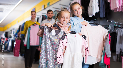Two happy sisters with parents satisfied with purchases in children clothing shop