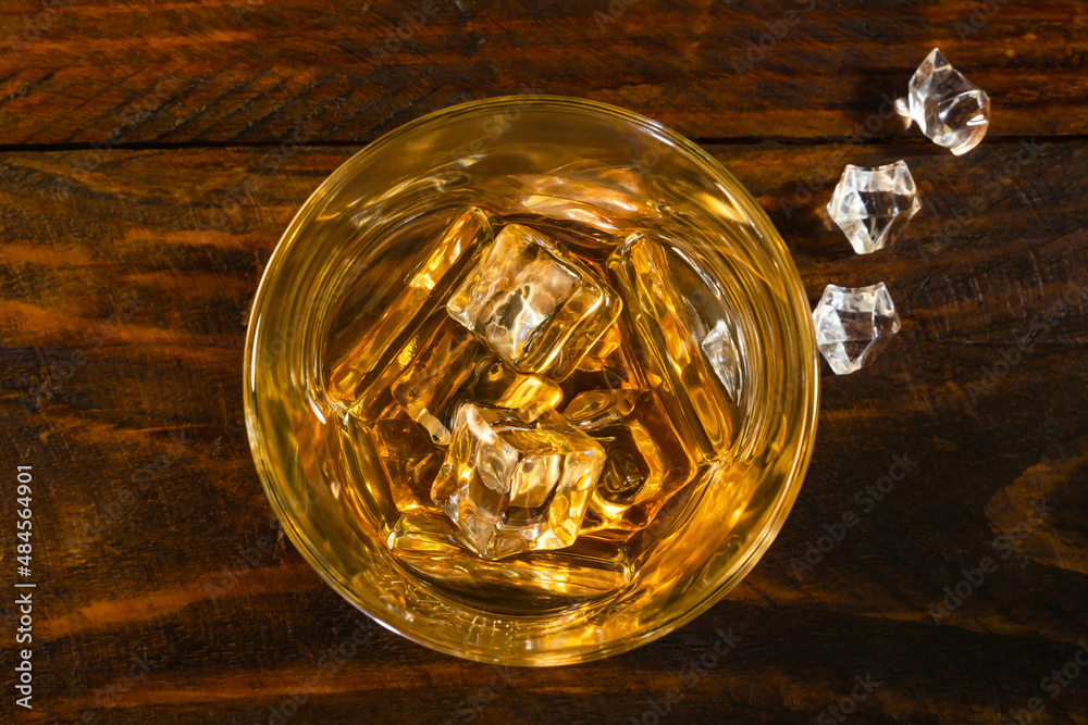 On a dark wooden background there are pieces of ice and a glass of whiskey on ice. Top view, close-up.