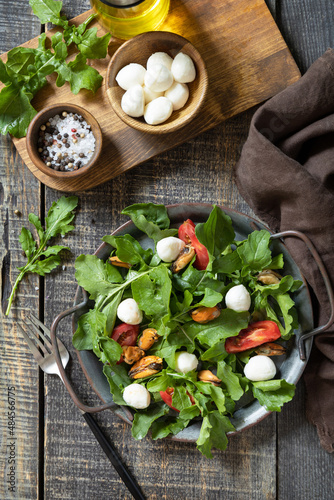 Healthy diet salad with arugula, mozzarella, mussels and vinaigrette dressing on a wooden table. Low calories keto dieting meal. Top view flat lay background.