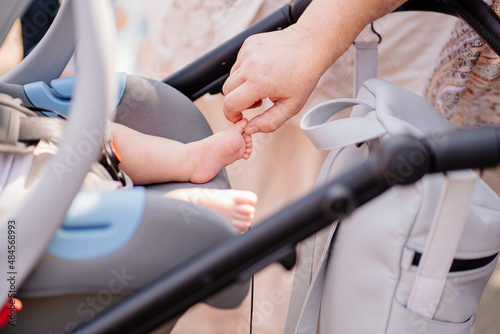 a woman's hand touches a leg of a little boy sleeps strapped in a stroller.