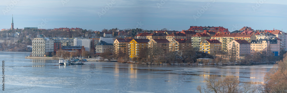 Panorama view over the island Lilla Essingen at an icy bay of the lake Mälaren with apartment houses, jetties and bridges a cold sunny winter day in Stockholm