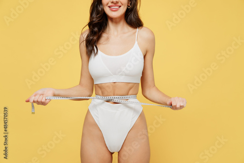 фотографія Cropped close up fun young woman 20s wearing white underwear with perfect fit body standing posing hold measure tape on waist isolated on plain yellow color background