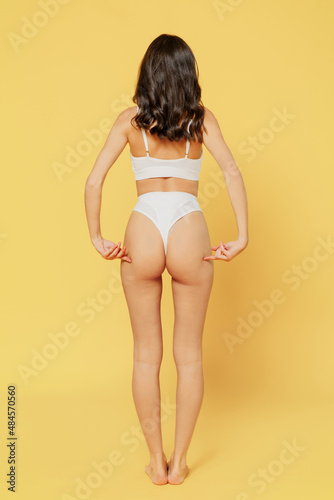 Full body back rear view confident beautiful young brunette woman 20s in white underwear with perfect fit figure point on buttocks isolated on plain yellow background. People female beauty concept