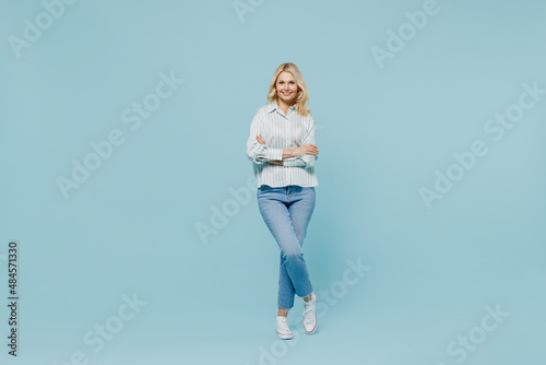 Full body elderly happy woman 50s wearing casual striped shirt looking camera hold hands crossed folded isolated on plain pastel light blue color background studio portrait. People lifestyle concept.