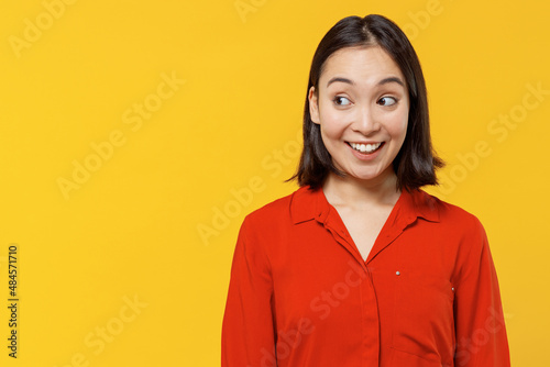 Charismatic stunning happy young woman of Asian ethnicity 20s years old wears orange shirt looking aside smiling isolated on plain yellow background studio portrait. People emotions lifestyle concept.