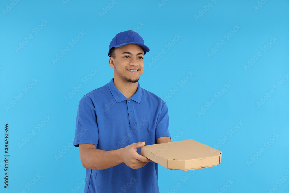 Young delivery man with pizza box on blue background