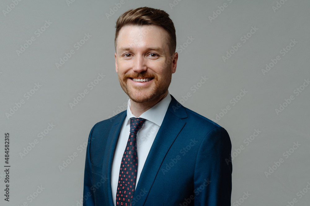 Cheerful male CEO in suit smiling at camera while posing against grey background Cheerful male CEO in suit smiling at camera while posing against grey background