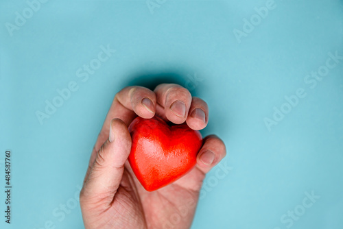 Fototapeta Naklejka Na Ścianę i Meble -  The red heart is squeezed by a man's hand. Top view on a blue background.