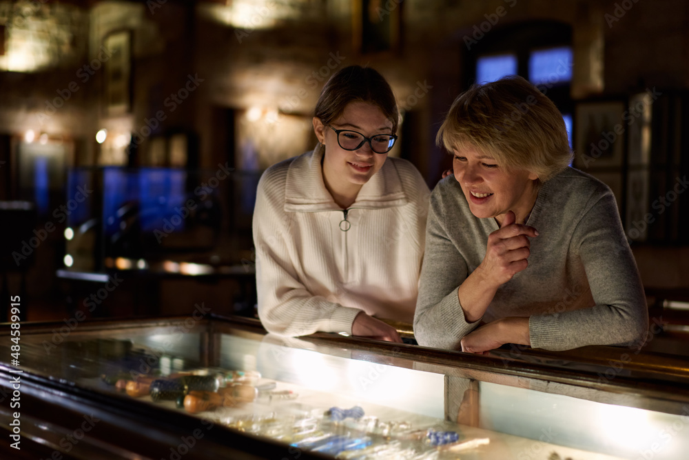 Girl with woman looking with interest at art objects under glass in museum