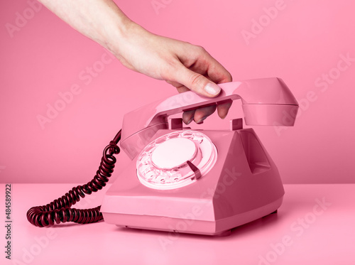 Woman hand holding retro phone handset on pink background and answering to call or hanging up. High quality photo