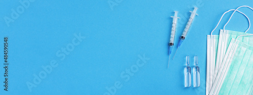 Medical masks, injection sharp needle and vial medications on clear blue background. Banner for website with copy space.