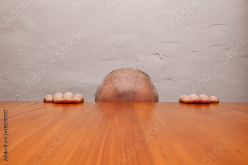 Fragment of male head extending above table lines and hands leaning against edge of table.