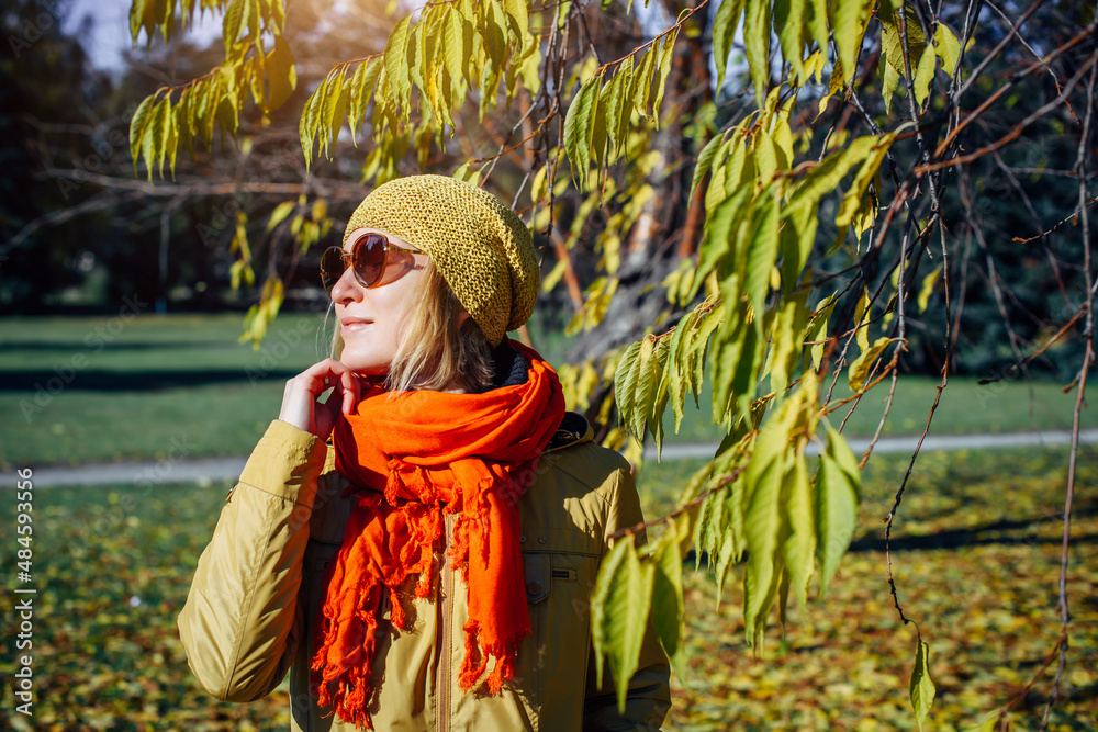 Portrait of attractive girl in sunglasses and red scarf on the background of yellow foliage in autumn park. Young woman enjoying walk on fall sunny day. Portrait of attractive girl in sunglasses and red scarf on the background of yellow foliage in autumn park. Young woman enjoying walk on fall sunny day.