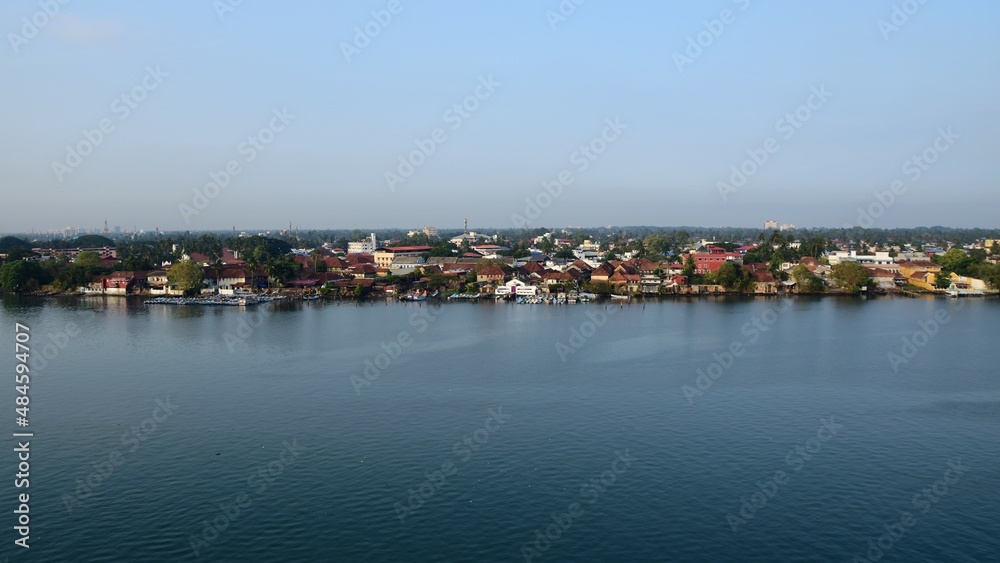Einfahrt in den Hafen von Cochin Indien mit Blick auf die Häuser am Hafenbeckenrand, sowie das Hinterland und Plastikmüll im Wasser