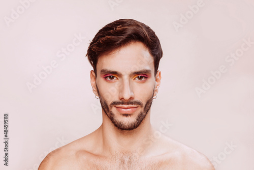 Portrait of gay man with beard, pink and yellow eyeshadow, no clothes. Beauty, make-up and skin care concept. Studio face shot, copy space.