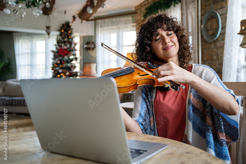 Woman student learns to play the violin online using a laptop.