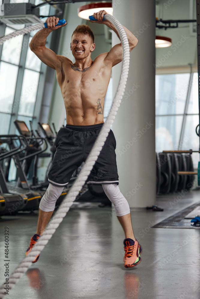 Front view of Attractive young fit and toned sportswoman working out with battle ropes. Motion blur