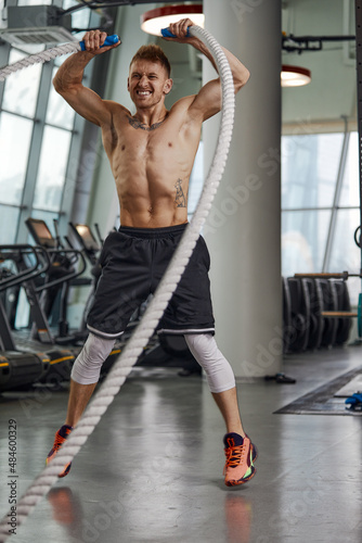 Front view of Attractive young fit and toned sportswoman working out with battle ropes. Motion blur