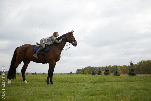 Beautiful young woman riding a horse on the field. Sideways to the camera. Freedom, joy, movement