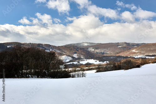 Winter mountain snowy landscape with forest. Beautiful blue sky with white cluster of clouds. Hills in the background. Nature background, wallpaper. Protected area Vrsatec, Slovakia.
