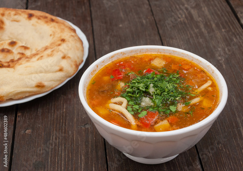 Soup lagman with herbs and flatbread on wooden table