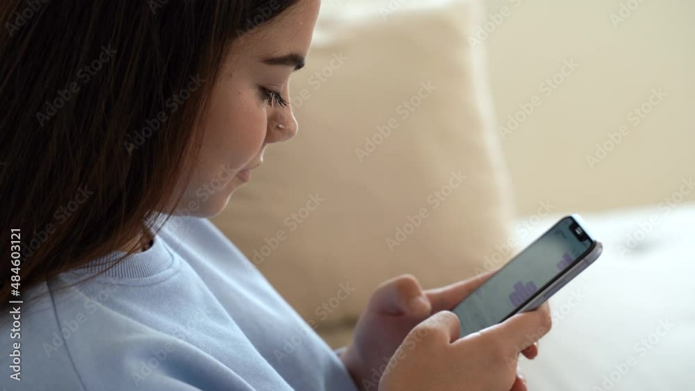 Beautiful and happy, smiling young teenage girl sit at sofa. Interact with phone application. Cute teenager typing message on mobile, chatting with friends on social networks. Content phone user. 4k Beautiful and happy, smiling young teenage girl sit at sofa. Interact with phone application. Cute teenager typing message on mobile, chatting with friends on social networks. Content phone user. 4k