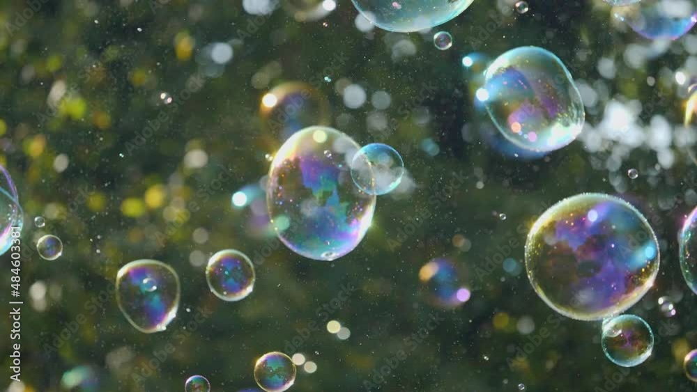 Slow-motion shot of glittering soap bubbles reflecting the sun rays in the park Slow-motion shot of glittering soap bubbles reflecting the sun rays in the park