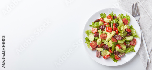 Salad with lettuce, cucumbers, tomatoes, olives and avocados in white plate on the table