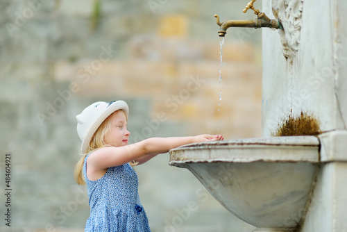 Young girl playing in drinking water fountain in Lucca city, known for its intact Renaissance-era city walls and well preserved historic center. Tuscany, Italy.