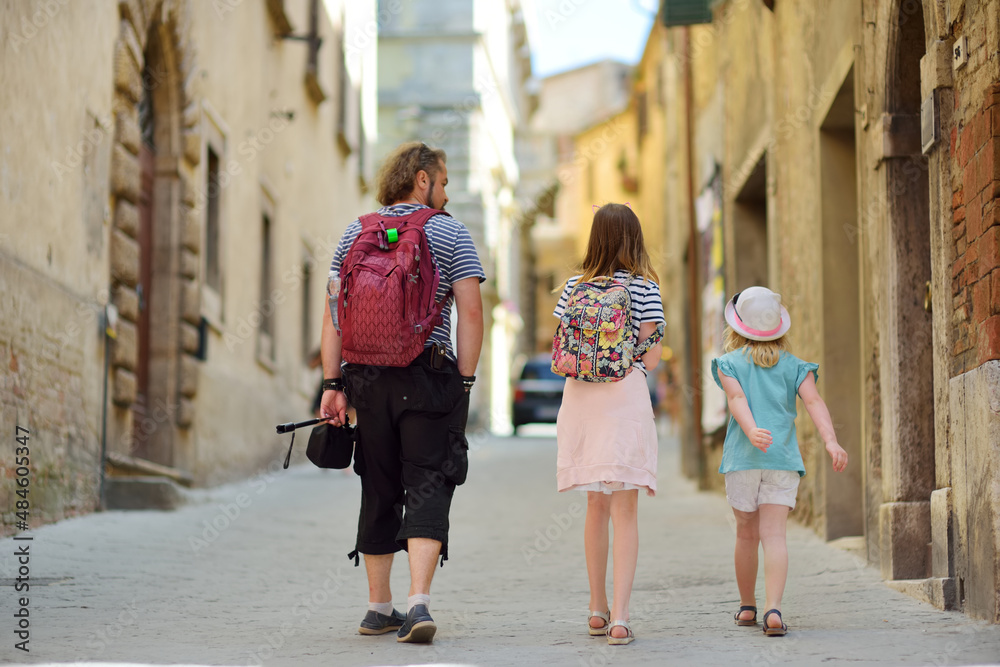 Father and daughters exploring old narrow streets of Montepulciano town, located on top of a limestone ridge surrounded by vineyards. Tuscany, Italy.