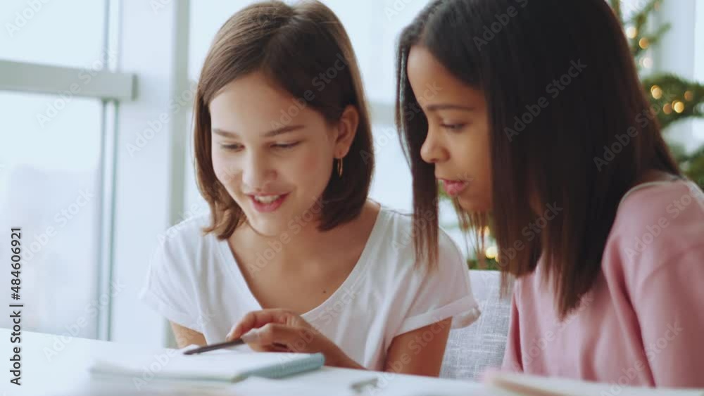 Two happy multiethnic sisters reading something from notepad at home Two happy multiethnic sisters reading something from notepad at home