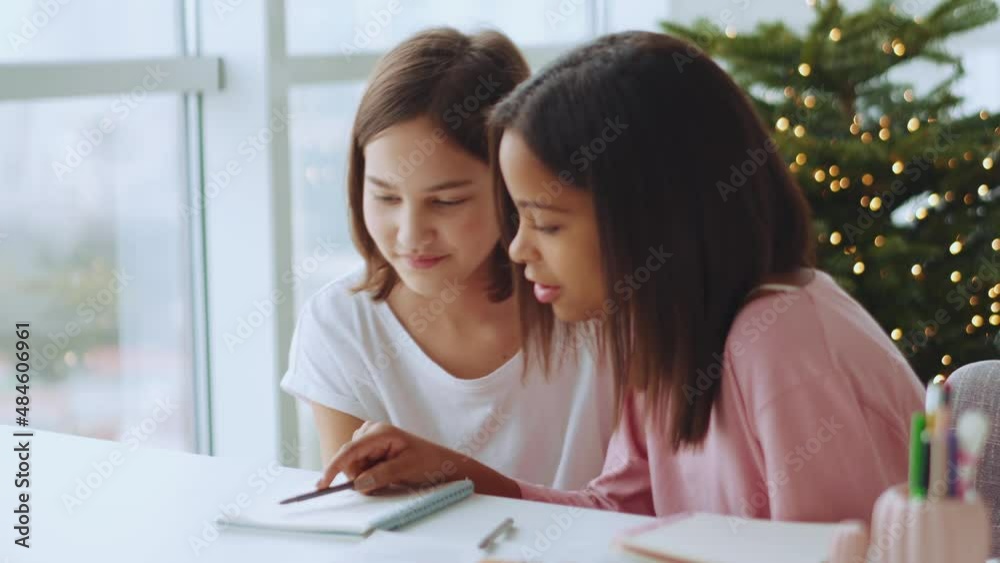 Two positive multiethnic sisters reading something from notepad at home Two positive multiethnic sisters reading something from notepad at home
