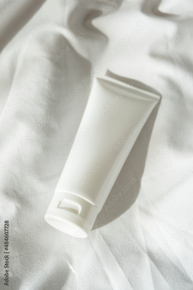 Plastic white tube for cream or lotion on light fabric background. Skin care cosmetic presentation with daylight and beautiful shadow. Beauty concept for face body care. Plastic white tube for cream or lotion on light fabric background. Skin care cosmetic presentation with daylight and beautiful shadow. Beauty concept for face body care.