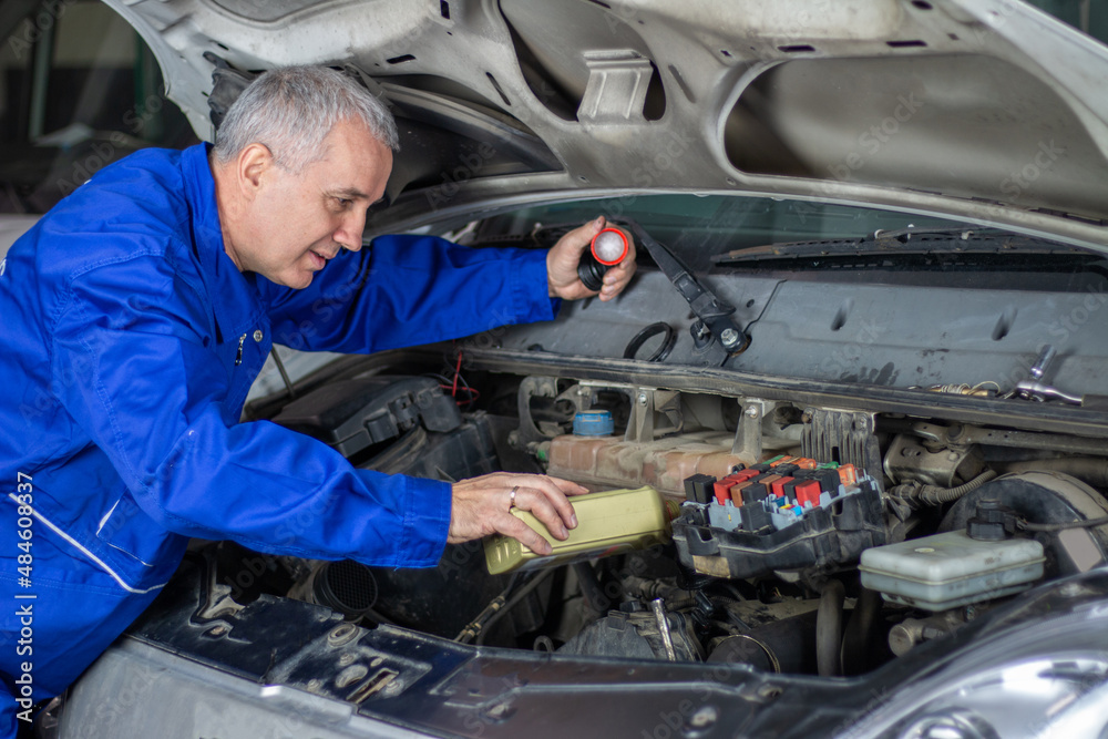 An experienced car mechanic changing oil on a car and pouring a motor oil during a car repair in auto mechanic service. An experienced car mechanic changing oil on a car and pouring a motor oil during a car repair in auto mechanic service.