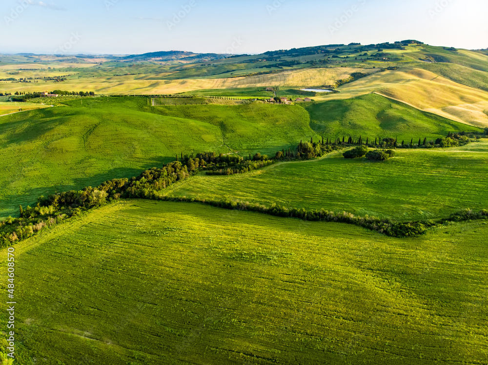 Stunning aerial view of green fields and farmlands with small villages on the horizon. Rural landscape of rolling hills, curved roads and cypresses of Tuscany, Italy. Stunning aerial view of green fields and farmlands with small villages on the horizon. Rural landscape of rolling hills, curved roads and cypresses of Tuscany, Italy.