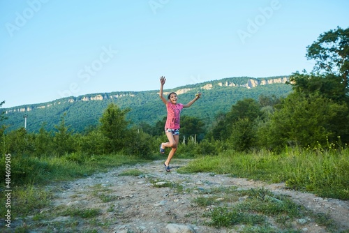 A girl runs along a country lane in summer with a bouquet of wild flowers in her hands. Happiness and a smile. There are mountains in the background.