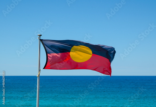 Australian aboriginal flag waving with blue sky and ocean water at the background. photo