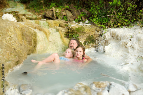 Family of three bathing in Bagni San Filippo, small hot spring containing calcium carbonate deposits, forming white concretions and waterfalls. Geothermal pools and hot springs in Tuscany, Italy.