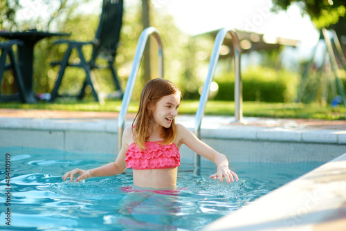 Cute young girl having fun in outdoor pool. Child learning to swim. Kid having fun with water toys. Family fun in a pool. Summer activities for family with kids. © MNStudio