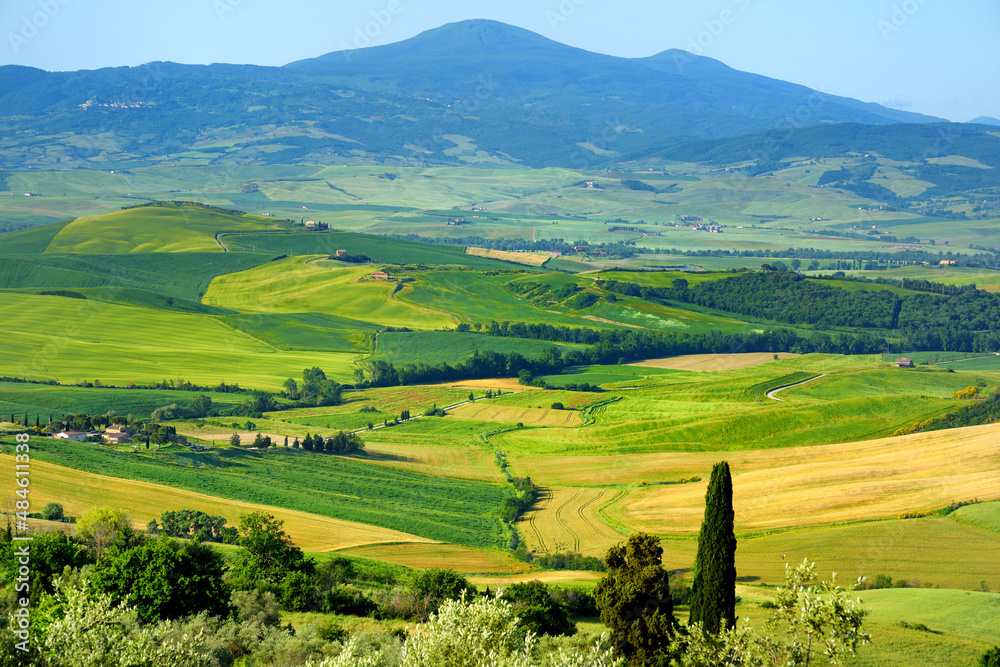 Stunning view of green fields and farmlands with small villages on the horizon. Rural landscape of rolling hills, curved roads and cypresses of Tuscany, Italy.