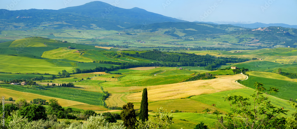 Stunning view of green fields and farmlands with small villages on the horizon. Rural landscape of rolling hills, curved roads and cypresses of Tuscany, Italy.