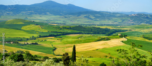 Stunning view of green fields and farmlands with small villages on the horizon. Rural landscape of rolling hills  curved roads and cypresses of Tuscany  Italy.