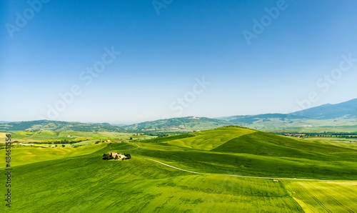 Stunning aerial view of green fields and farmlands with small villages on the horizon. Rural landscape of rolling hills  curved roads and cypresses of Tuscany  Italy.