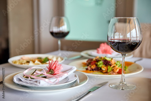A served restaurant table with glasses of red wine and appetizer awaits guests. Close-up, selective focus