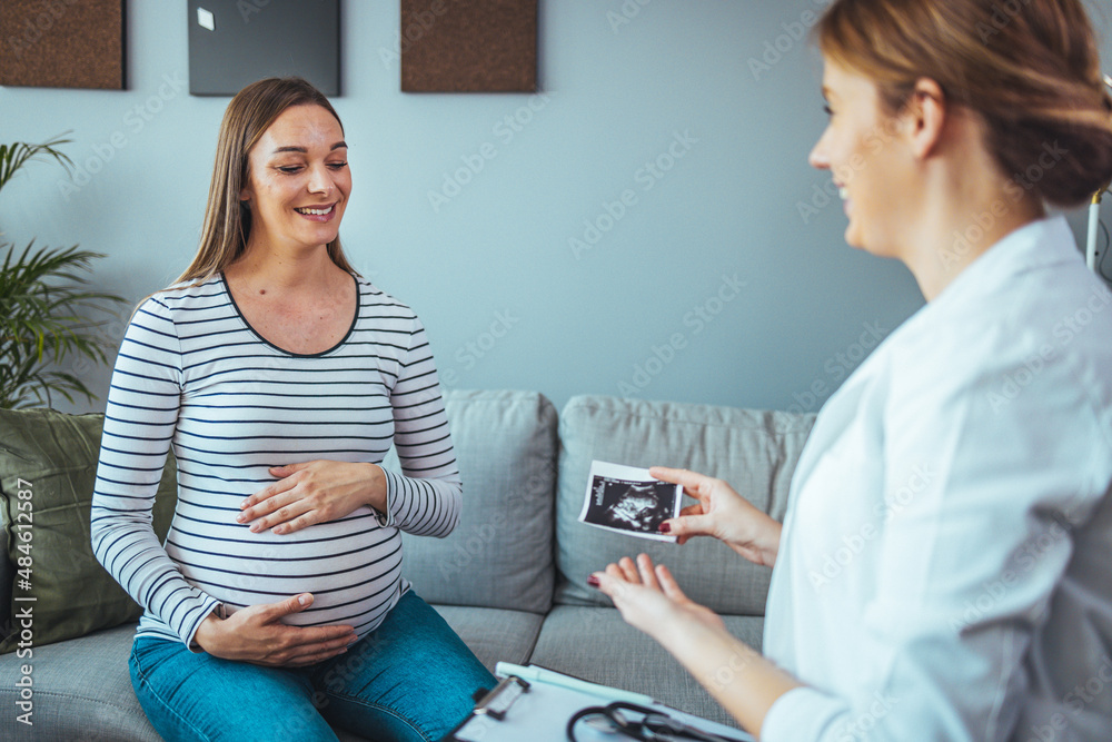 The doctor shows a sonographic picture of the baby while sitting on the sofa at home, shows the first photo of her child, enjoys a happy maternity leave. The doctor shows a sonographic picture of the baby while sitting on the sofa at home, shows the first photo of her child, enjoys a happy maternity leave.