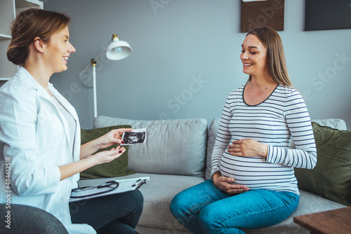 The doctor shows a sonographic picture of the baby while sitting on the sofa at home, shows the first photo of her child, enjoys a happy maternity leave. photo