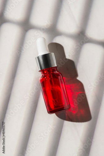 Red glass bottles with dropper pipette with serum or essential oil on a white background. Skincare cosmetic with beautiful shadows. Beauty concept for face body care.