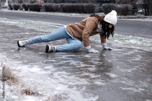 Young woman trying to stand up after falling on slippery icy pavement outdoors photo